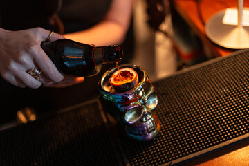 Bartender girl makes alcoholic cocktail and pours alcohol into glass skull with passion fruit