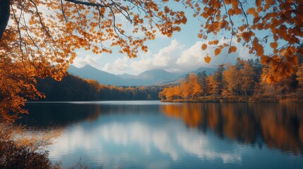 Fototapeta premium Stunning autumn lake view with vibrant leaves and mountains reflecting on calm water under a bright sky.