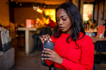 Young woman stirring reusable coffee cup in cafe