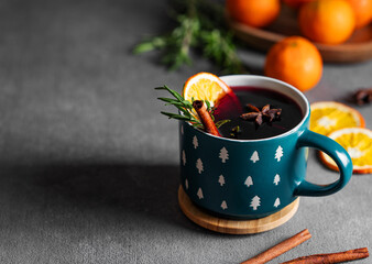 Mulled wine with orange, cinnamon and rosemary in a cup on a dark background with tangerines.