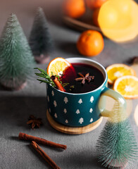 Mulled wine with orange, cinnamon and rosemary in a cup on a dark background with tangerines, fir...
