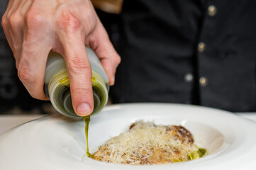 A hand pours green olive oil over a beautifully plated dish with cheese. The elegant presentation showcases culinary artistry, perfect for food-related content or gourmet cooking themes.