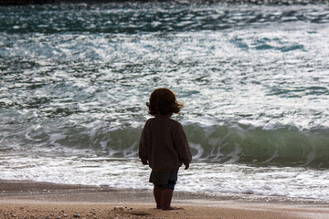 the silhouette of a unrecognizable child from behind while observing the sea, symbol of immensity