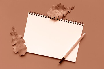 Mockup. White sheet of paper, fallen autumn oak leaves and pen on Mocha and Mousse, brown background. Notebook for notes. Demonstrating color of 2025 year