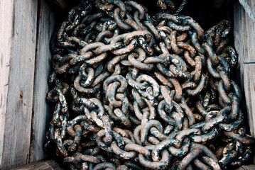 Large rusty metal chain from ship anchor lying in wooden box, rebar texture
