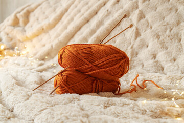 Two red thread spools and wooden knitting needles on blanket, shiny lights on background