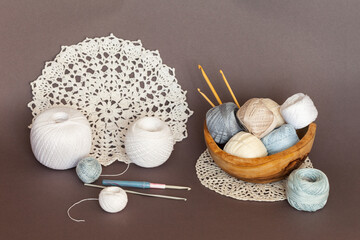 Close-up of wooden bowl with skeins of light natural cotton yarn for crocheting, crochet hooks and...