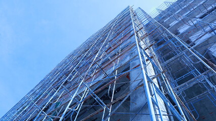 Scaffolding next to a new building. Building under construction with metal scaffolding set beside a commercial or residential building on a crane and sky background with copy space and selective focus