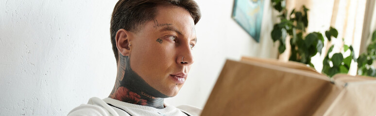 Man with tattoos deeply engaged in his book while sitting comfortably indoors.