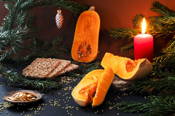 Sliced elongated pumpkin on a festive table with Christmas decorations, pine branches, candle, and...
