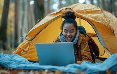 Black woman working on laptop lying in a camp tent. Workation concept, digital nomad, flexible productivity, travel, adventure, location independent, remote mobile office, exploring balance, getaway