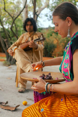 Indian musician in traditional clothes playing sitar festive season outdoor home. Woman in traditional saree hand lighting Diya lamp during Diwali festival. Happy greeting photo. Part of a series