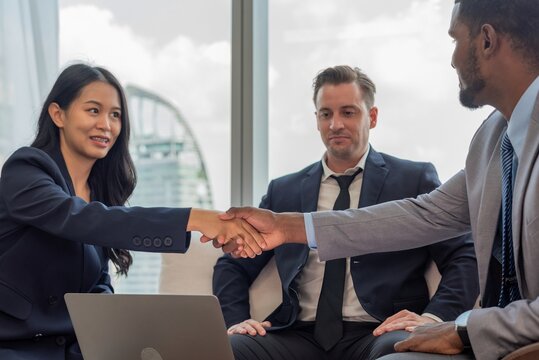 A diverse group of business professionals in suits shaking hands in an office.