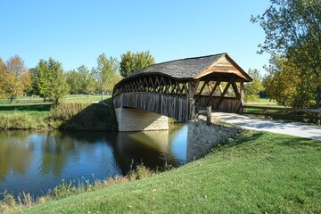 Fototapeta premium Covered bridge with wooden beams inside, crossing a quiet creek on a sunny day