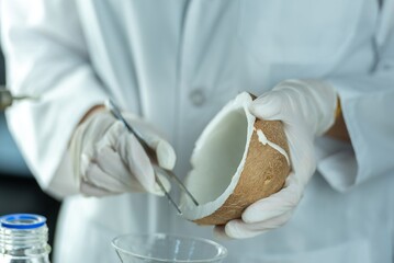 A gloved scientist carefully examines a coconut with a pair of tweezers.