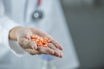 A doctor holding a handful of orange pills in the palm of their hand.