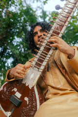 Indian musician in traditional clothes playing sitar festive season outdoor home. Happy Diwali...