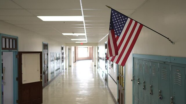 Brightly lit hallway in a school featuring rows of lockers and an American flag hanging above. The space reflects the calm before the day's activities begin.