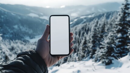 A hand holding a smartphone with a white screen mock-up, standing on a snowy mountain peak