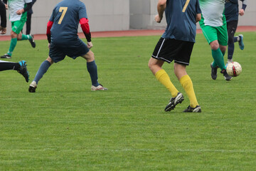 Dynamic fragment of a soccer game on the football field, defenders of the team against a player with the ball, footballers in green and blue uniforms on the football field