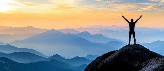 As the sun rises over the mountains, a man at the peak enjoys his newfound freedom.
