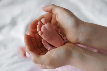 A baby's foot is being held in a mother's hand. The baby is pink and he is a newborn. Concept of warmth and tenderness, as the mother is holding her baby close to her chest