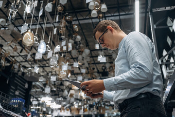 Many chandeliers on the ceiling. Male hardware store worker in indoors