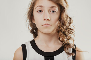 Serious young girl with long brown wavy hair looking at camera
