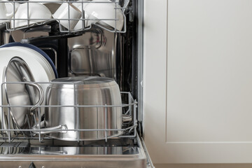 Built-in dishwasher full of clean dishes with its door open, white utensil and a stainless still...