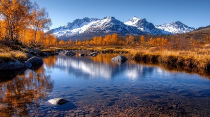 Obraz premium Snow-capped mountains rise above a calm river reflecting autumn trees and a clear blue sky.