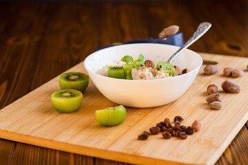 cooked oatmeal with kiwi, honey and nuts in a bowl on a wooden table