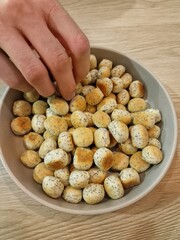 A hand reaching into a bowl filled with biscuits. A bowl of Kūčiukai (Lithuanian traditional Christmas Eve biscuits with poppy seeds). Close-up 