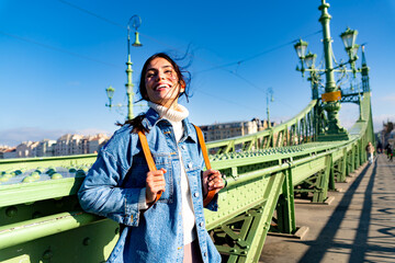 Fototapeta premium A smiling woman looking around joyfully, with her hair blowing in the wind, enjoying the moment on the bridge