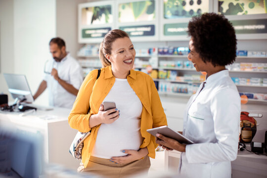 Female pharmacist helping pregnant woman in drug store