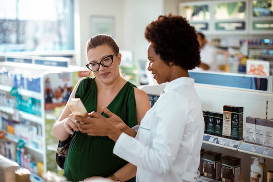 Female pharmacist helping pregnant woman in drug store