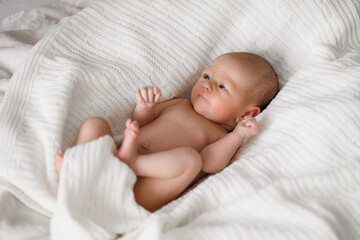 A baby is laying on a white blanket. The baby is naked and has a blue face. The baby is looking at the camera