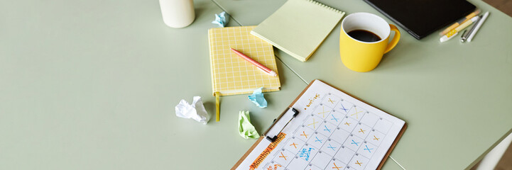 Website header shot of monthly planner with ticked off events resting on working desk cluttered...