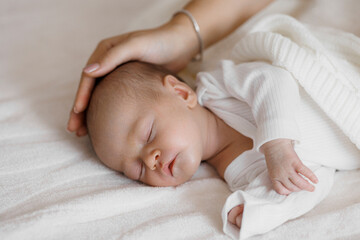 A baby is sleeping on a bed with a blanket over it. The baby is covered with a blanket and has its head resting on the mother's shoulder. Concept of warmth and comfort