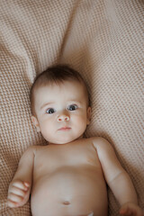 A baby is laying on a bed with its eyes wide open. The baby's face is the main focus of the image, and it is curious or surprised. The bed is covered in a blanket