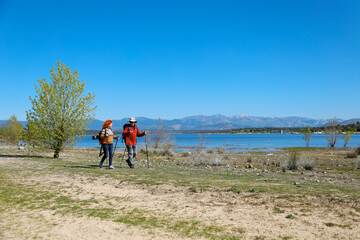 Hikers walking along lake shore with mountain view on sunny day