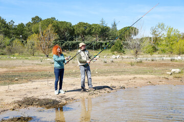 Couple fishing together on sunny day by the lake shore