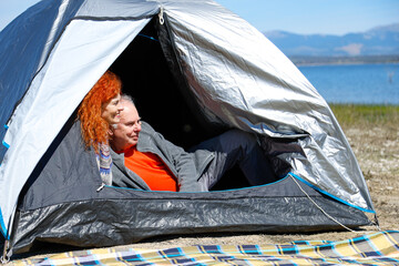 Senior couple relaxing in tent by lake enjoying camping trip