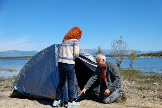 Senior couple setting up tent by lake on sunny day - Powered by Adobe