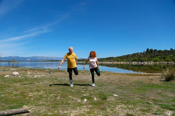 Senior couple stretching legs by the lake on sunny day