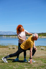 Senior man stretching with trainer by the lake