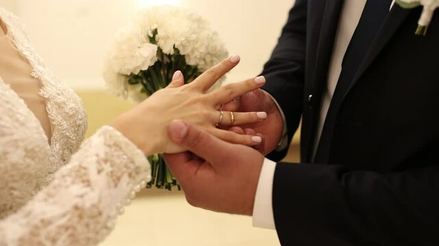 the groom puts a golden wedding ring on the bride's hand