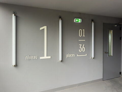 Indoor parking lot signage on a gray wall indicating level one and capacity details with illuminated vertical lights and emergency exit signage.
