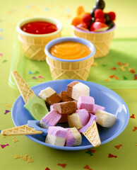Home made ice cream for children birthday party. A plate features an assortment of colorful ice cream squares alongside bowls of syrup and fruit.