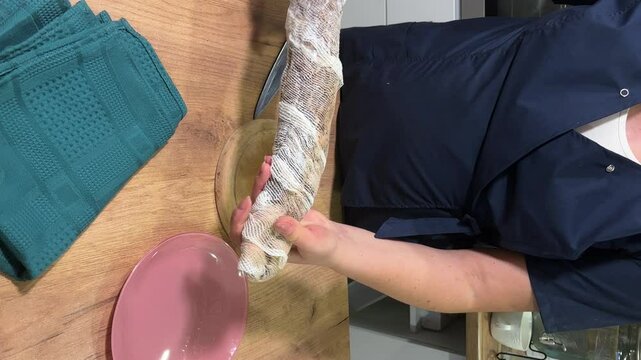 A woman is removing the cheesecloth that the cured pork is wrapped in. She makes a loin, dried pork tenderloin, processing pork at home. Vertical video.