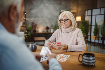 senior wife play cards with husband on wooden table at home